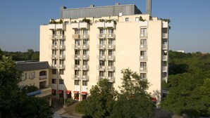A multi-story hotel with balconies, a flat roof, and a garden area in front.