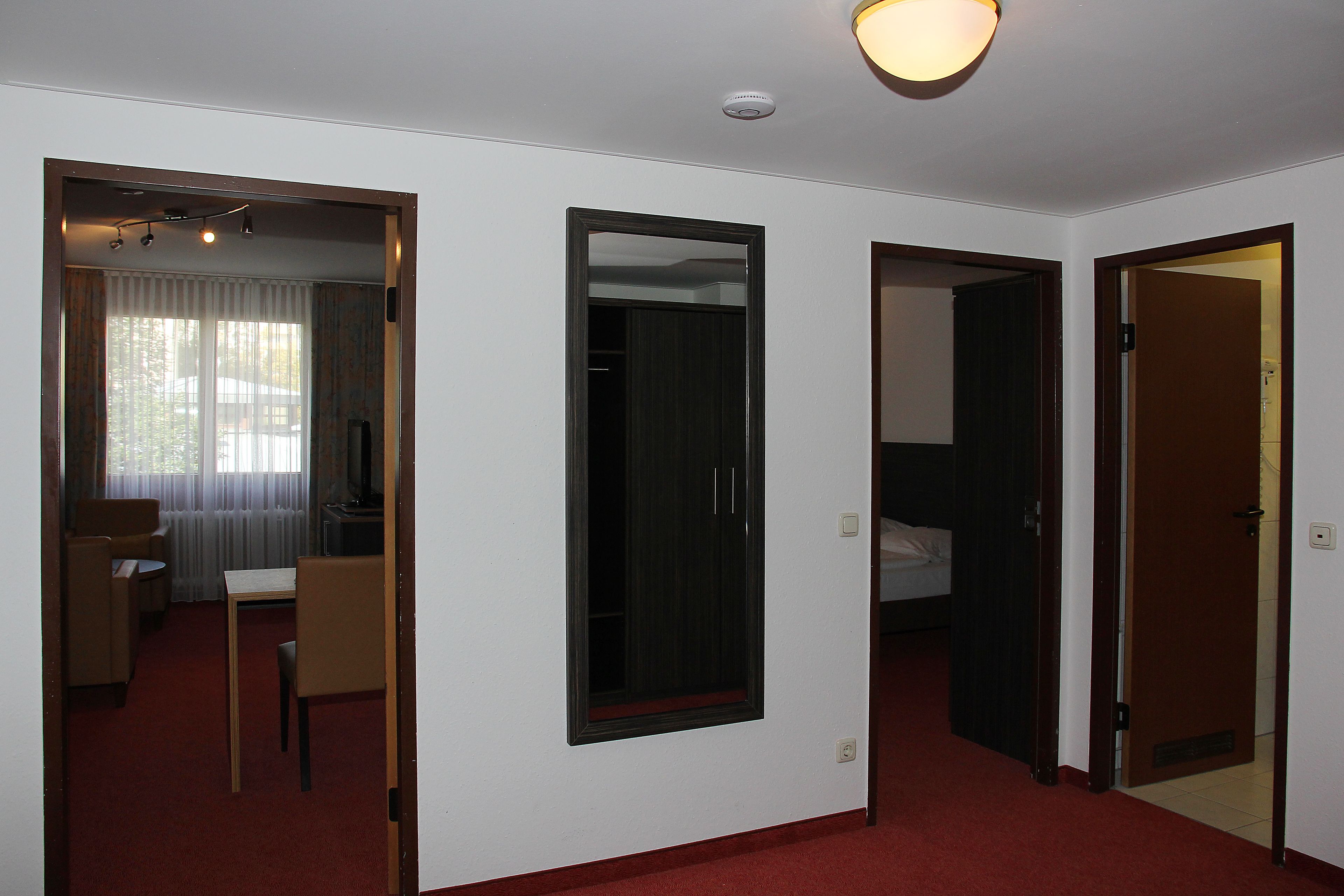 A hotel room with a bed, a desk, and a chair. There is a mirror on the wall and a door leading to another room.