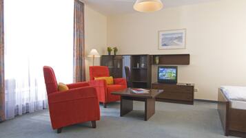 Una habitación de hotel con un sillón rojo, una mesa de centro de madera, un televisor, una cama y un cuadro en la pared.