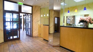 A hotel lobby with a reception desk, a mirror, and a tiled floor.