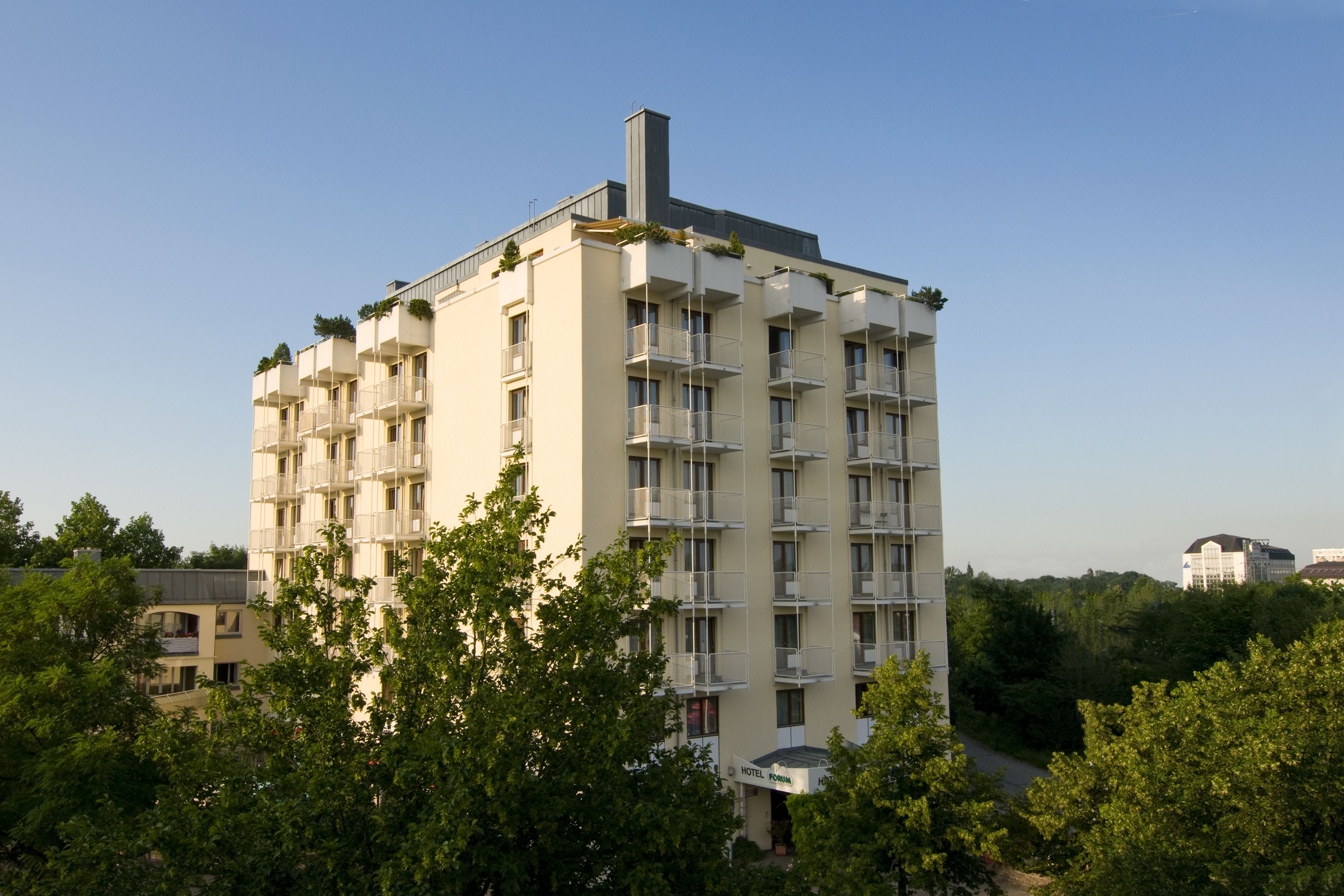 Un hôtel à plusieurs étages, doté de balcons et entouré d’arbres.