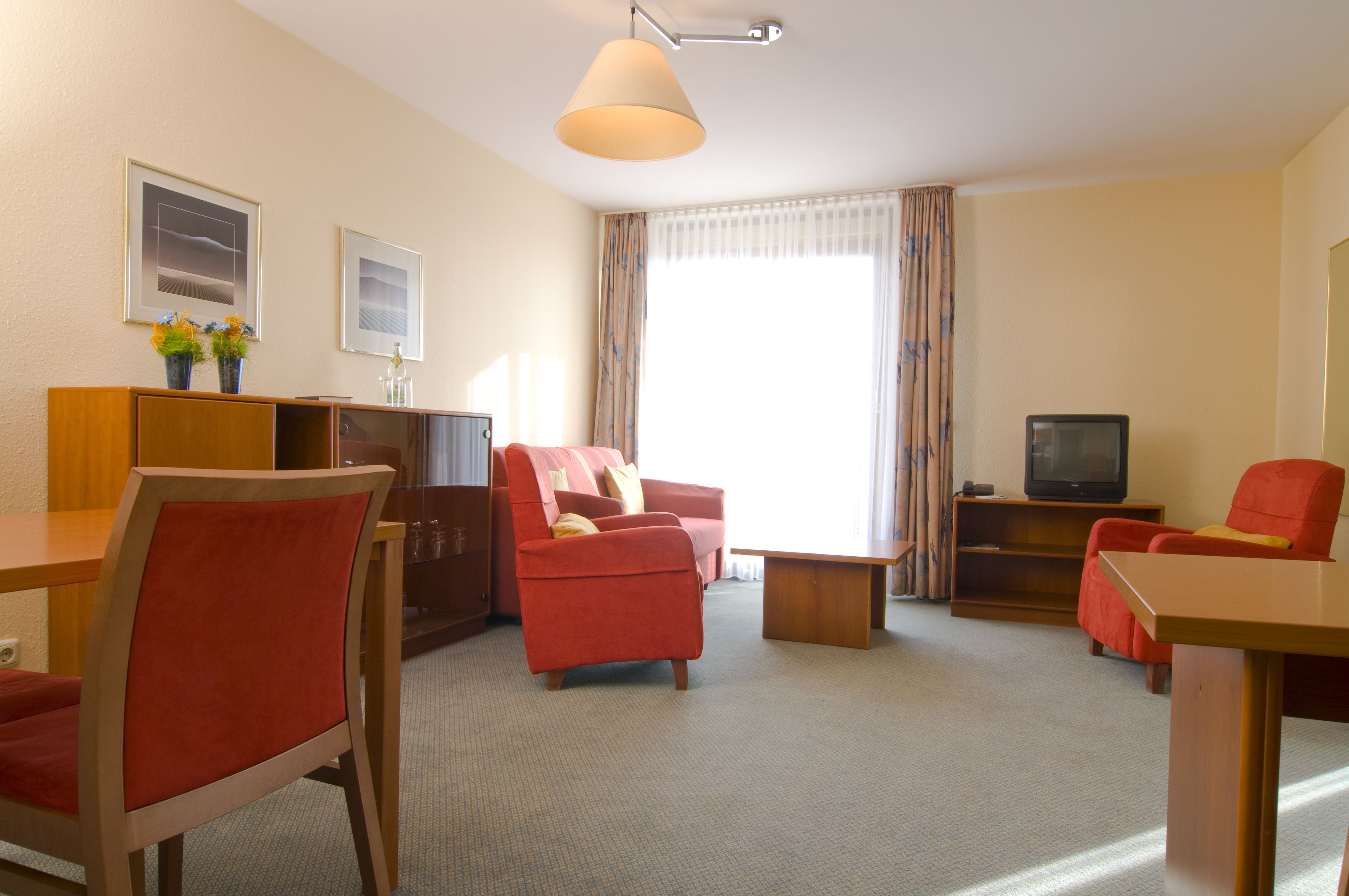 A hotel room with a dining area, a sofa, a TV, and a window with curtains.