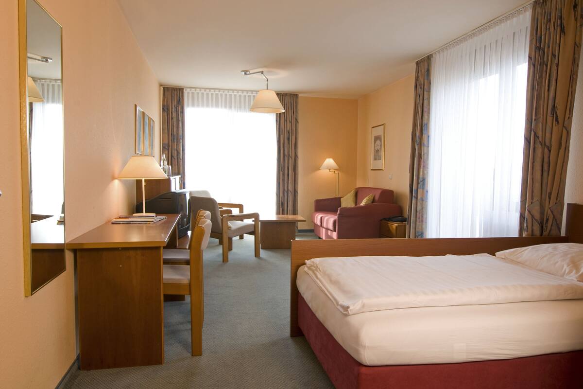 A hotel room with a bed, a desk, a chair, a sofa, and a lamp.