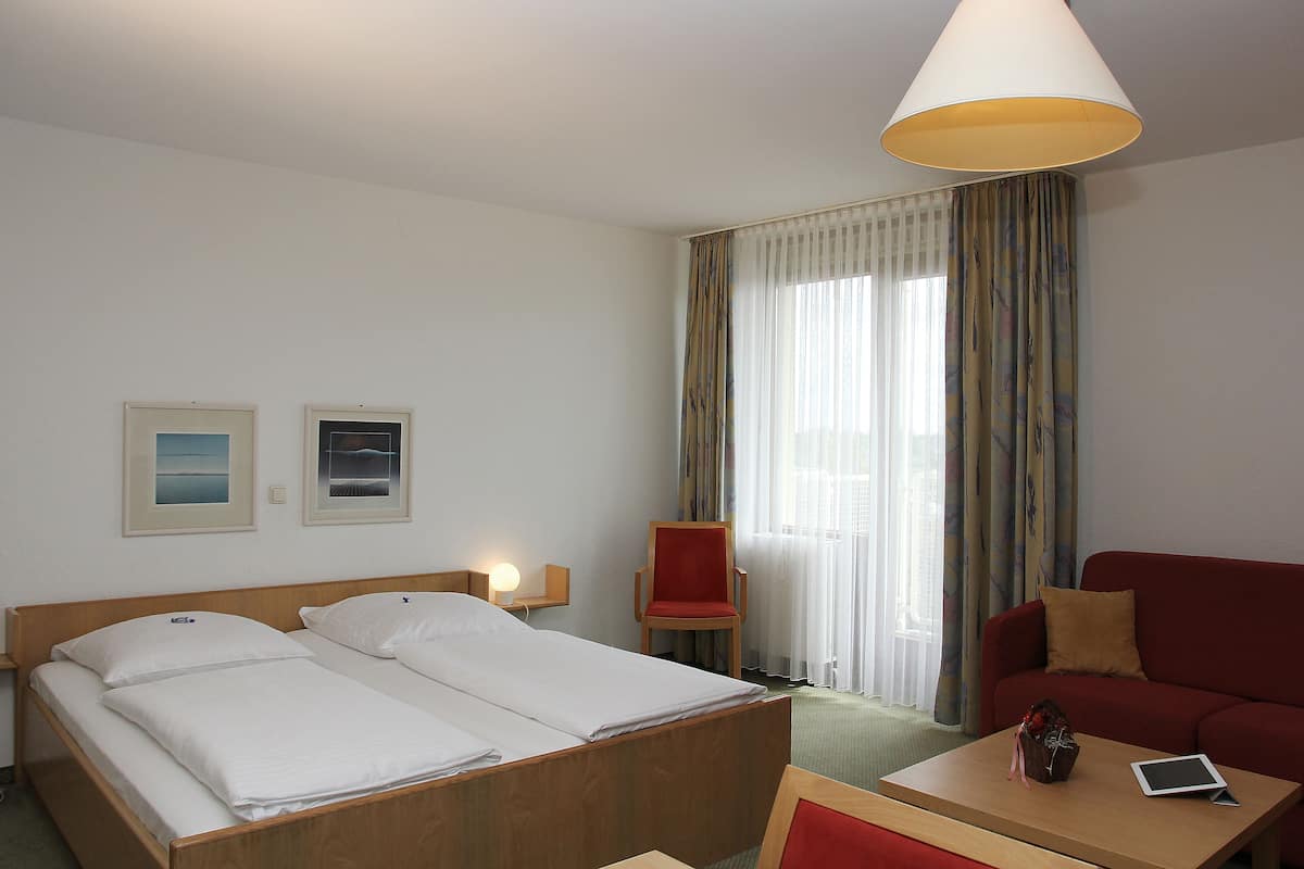 A hotel room with a bed, a red armchair, a red sofa, a small table, and a lamp.