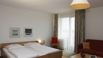 Una habitación de hotel con una cama, un sillón rojo, un sofá rojo, una mesita y una lámpara.