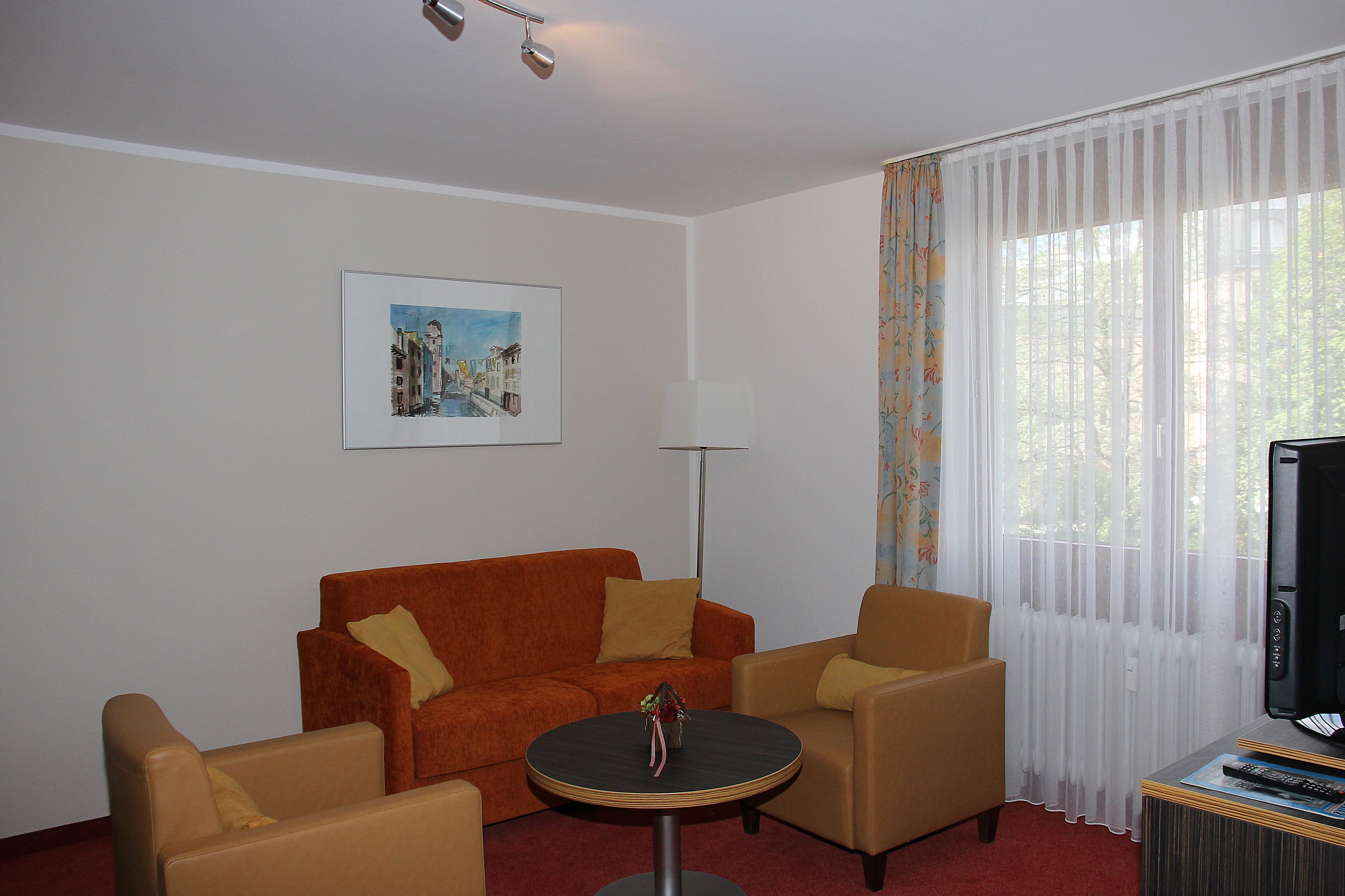 Una habitación con un sofá rojo, dos sillones, una mesita redonda, un televisor y un cuadro en la pared.