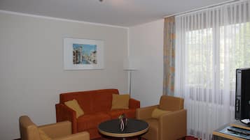 Una habitación con un sofá rojo, dos sillones, una mesita redonda, un televisor y un cuadro en la pared.