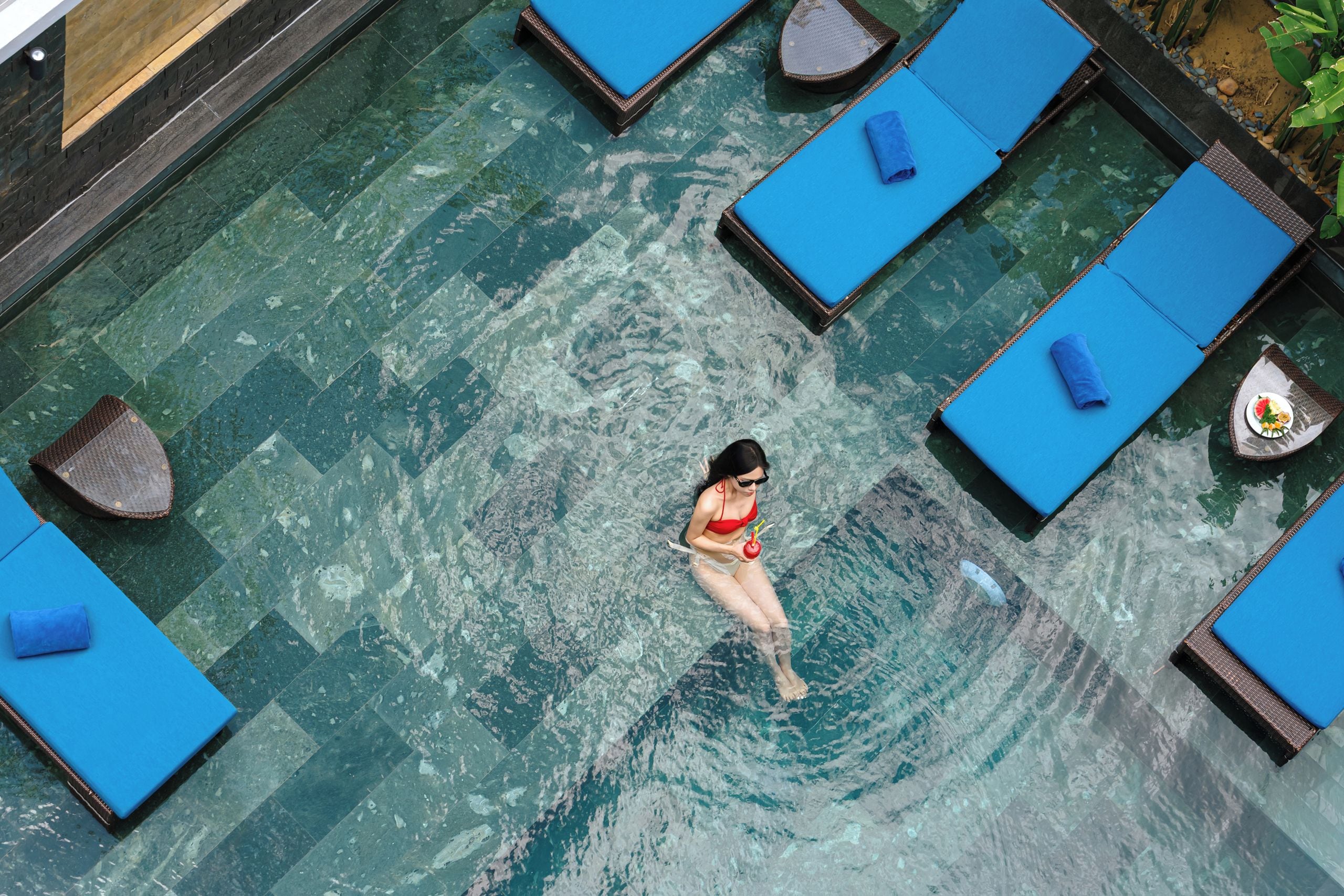 A swimming pool with multiple lounge chairs and a person swimming.