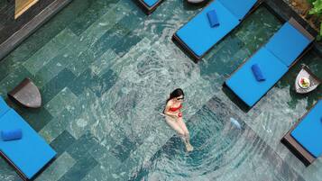A swimming pool with multiple lounge chairs and a person swimming.