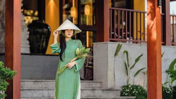 Una mujer vestida con traje tradicional posa bajo un letrero de hotel.