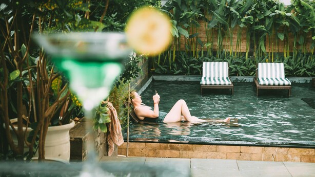 A pool area with lounge chairs and a glass of a green beverage.