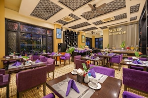 A dining area with purple upholstered chairs and tables, a ceiling fan, and a wall with the text "SILVER RIVERSIDE". - Royal Riverside Hoi An Hotel (Da Nang)