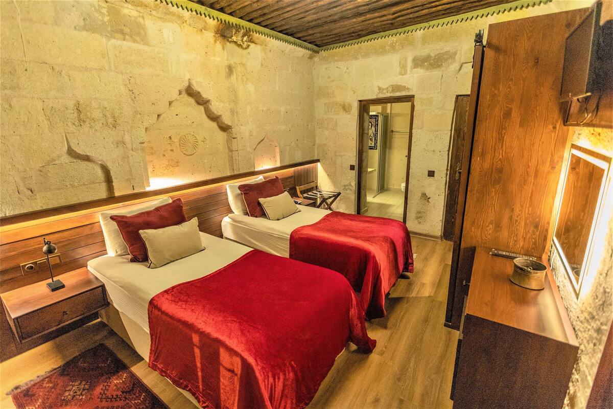 A room with two beds, wooden headboards, a small table, and a mirror.