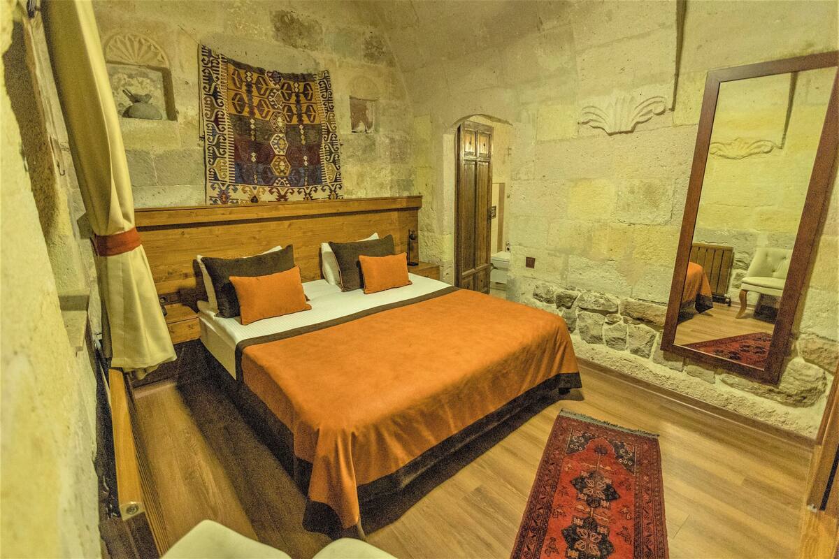 A bedroom with a wooden bed, a headboard, a large mirror, and a stone wall.