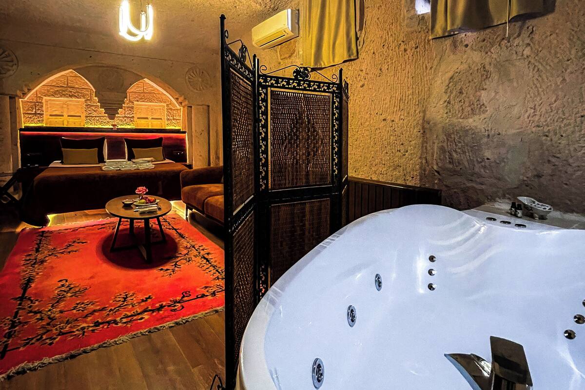 A room with a large bathtub, a wooden floor, a red carpet, and a bed with a headboard.
