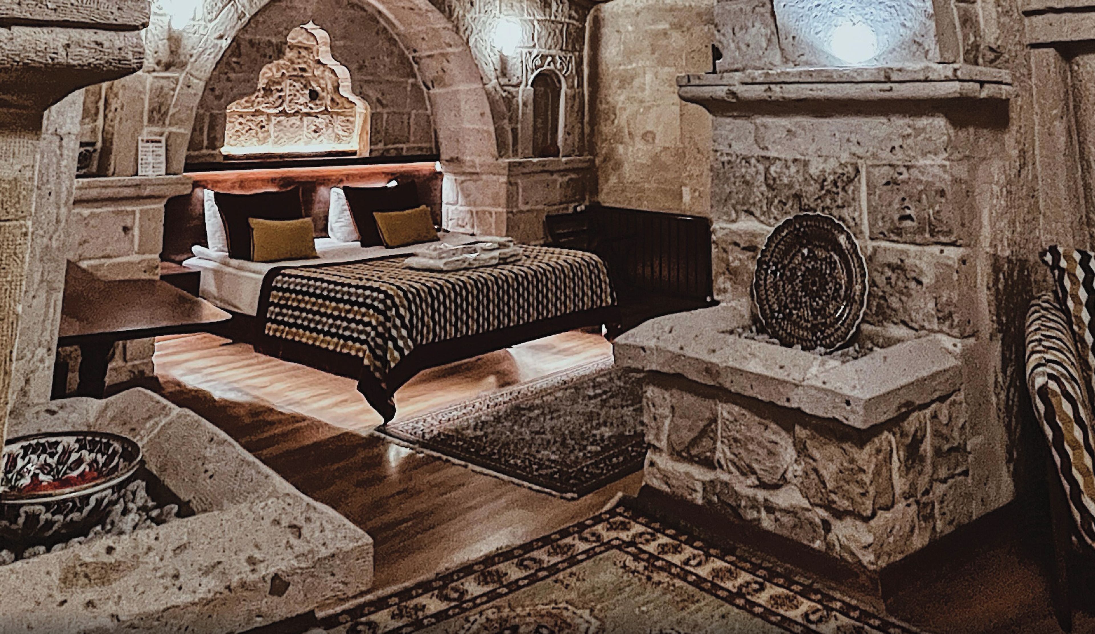 A stone-walled room with a bed, a fireplace, and a stone shelf.