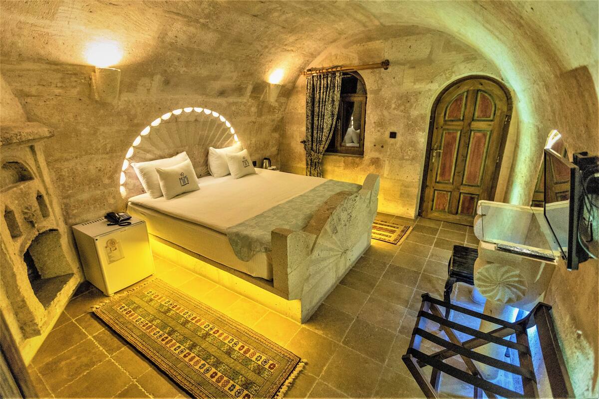 A bedroom with a bed, bedside table, lamp, and a view of the outside.