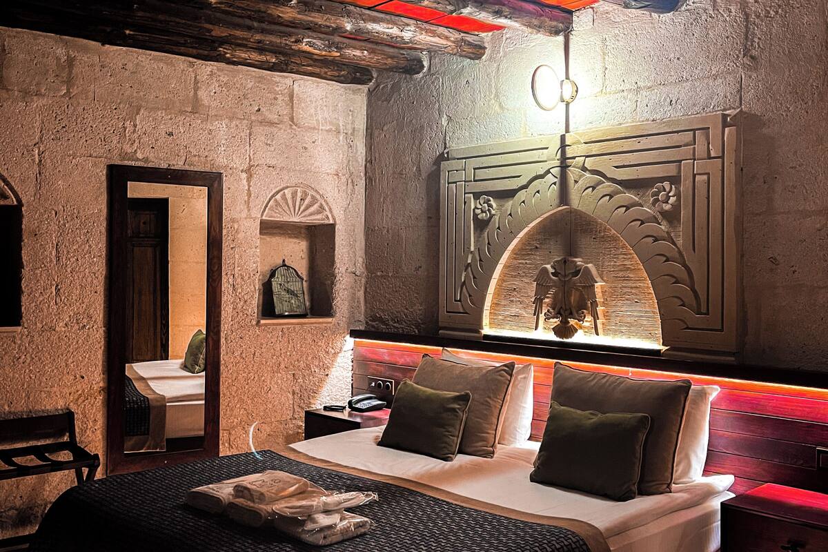 A bedroom with a large bed, a wooden bench, a mirror, and a wall-mounted artwork.