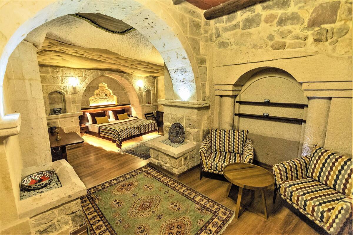 A cozy room with a stone fireplace, a bed with patterned bedding, a patterned armchair, and a small table.