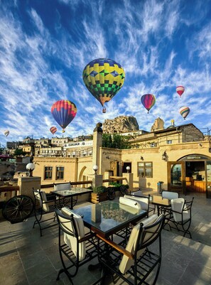 An outdoor seating area with tables and chairs, surrounded by a cityscape with buildings and a rocky hill in the background. - Mimi Cappadocia Butik Otel (Nevsehir)