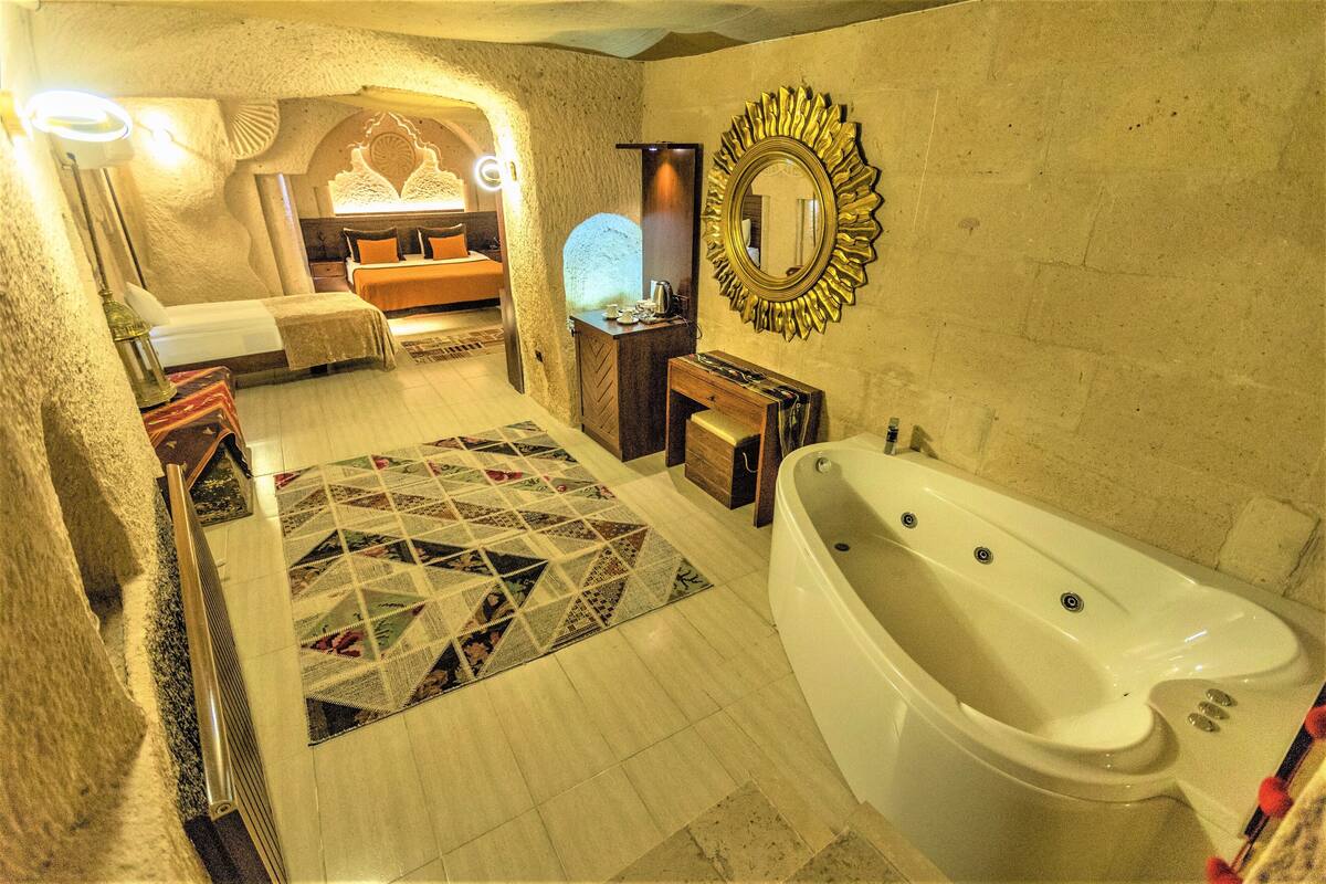 A bathroom with a large bathtub, a mirror with a sunburst frame, and a patterned rug on the floor.
