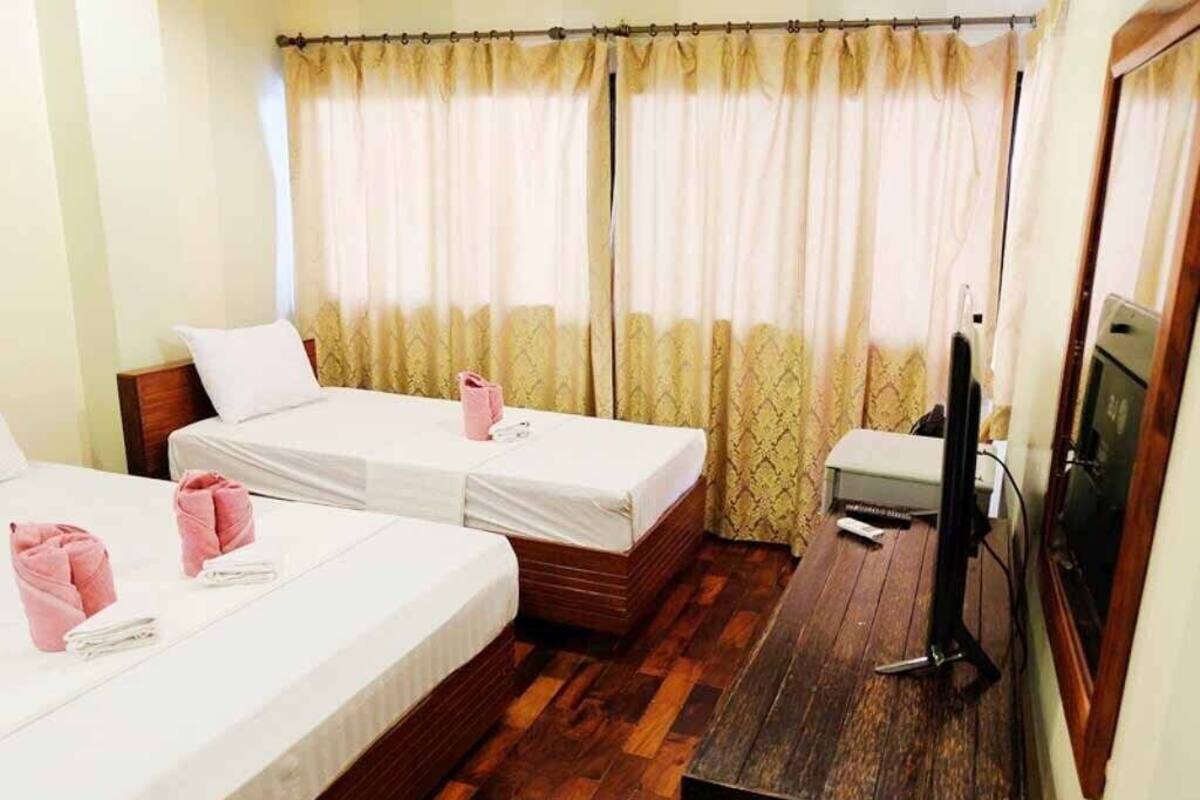 Ein Hotelzimmer mit zwei Einzelbetten, einem Holztisch, einem Fernseher und einem Fenster mit Vorhängen.