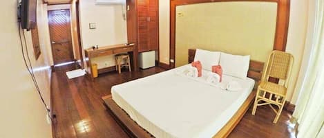 Habitación de hotel con una cama grande, cabecero de madera, un escritorio pequeño y una silla.