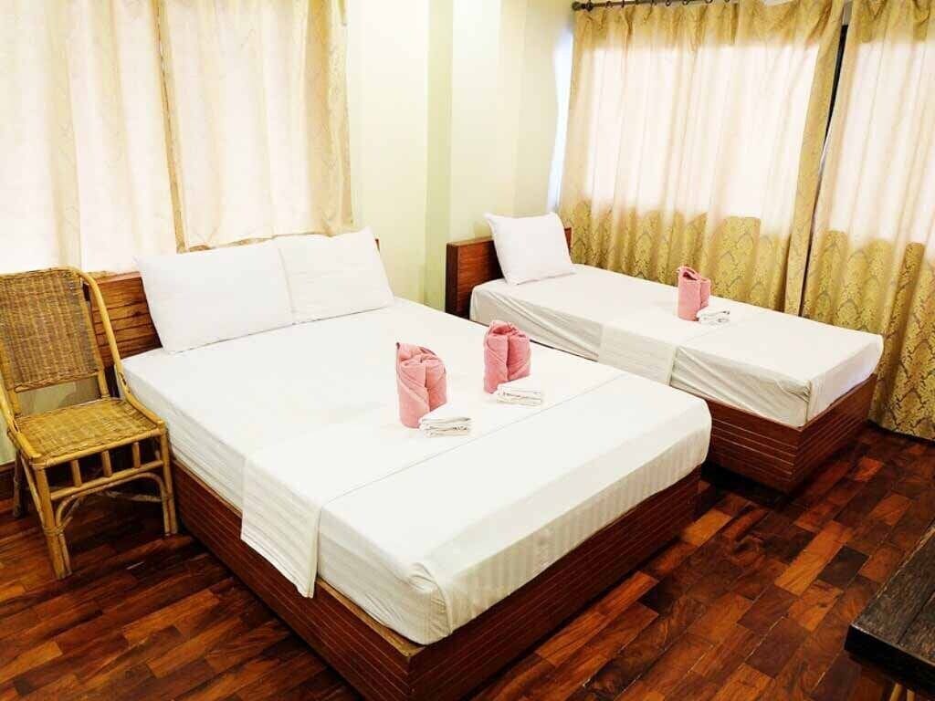 A hotel room with two single beds, wooden flooring, and a wicker chair.