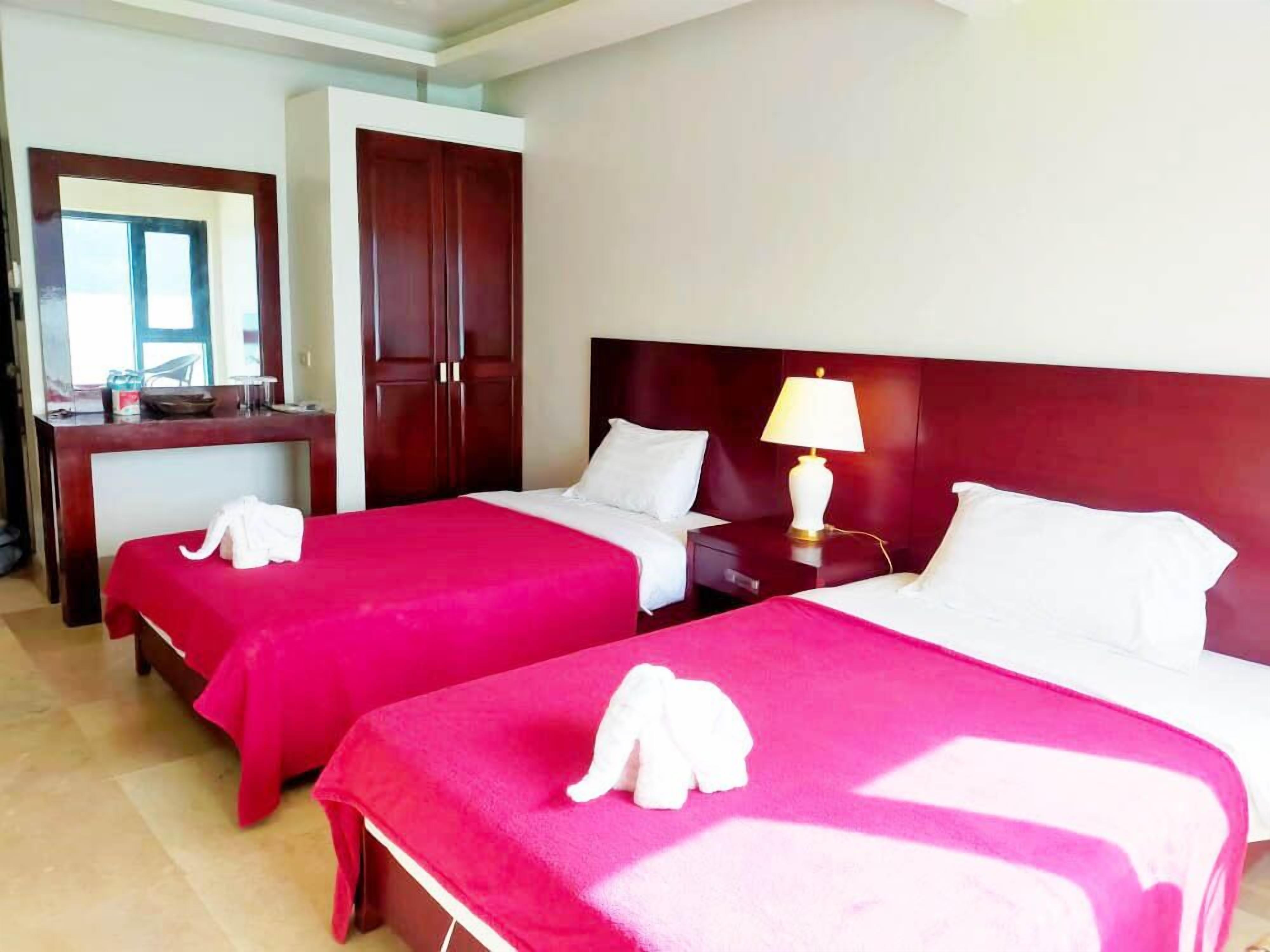 A hotel room with two beds, a desk, and a wardrobe.