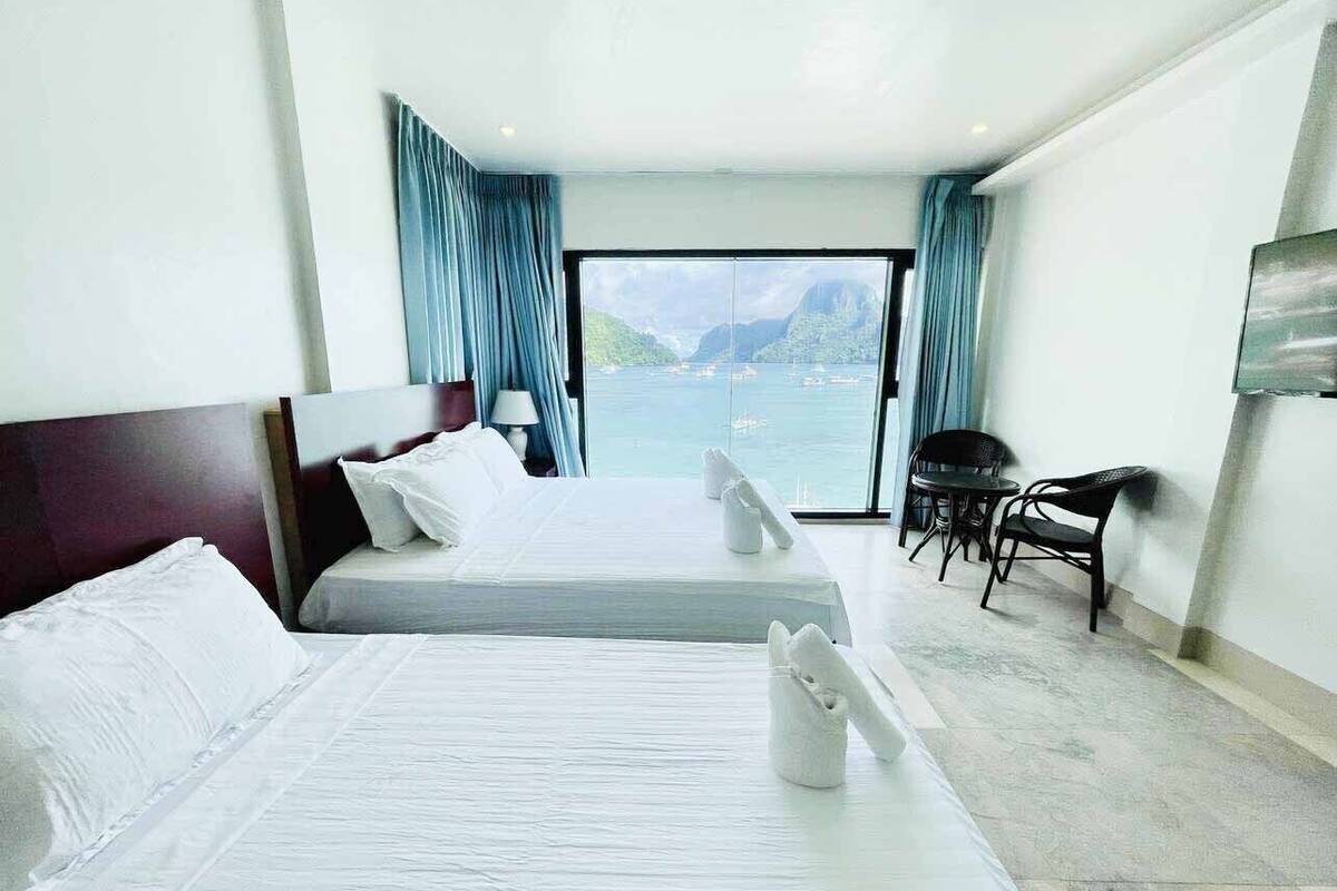 Ein Hotelzimmer mit zwei Betten, Meerblick und einem Essbereich mit Stühlen.