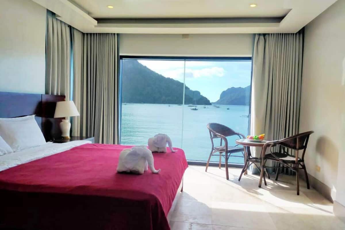 Ein Hotelzimmer mit einem großen Bett, einem kleinen Tisch mit Stühlen und Meerblick durch ein großes Fenster.