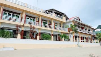 A multi-story hotel with balconies, a flat roof, and a sandy ground area.