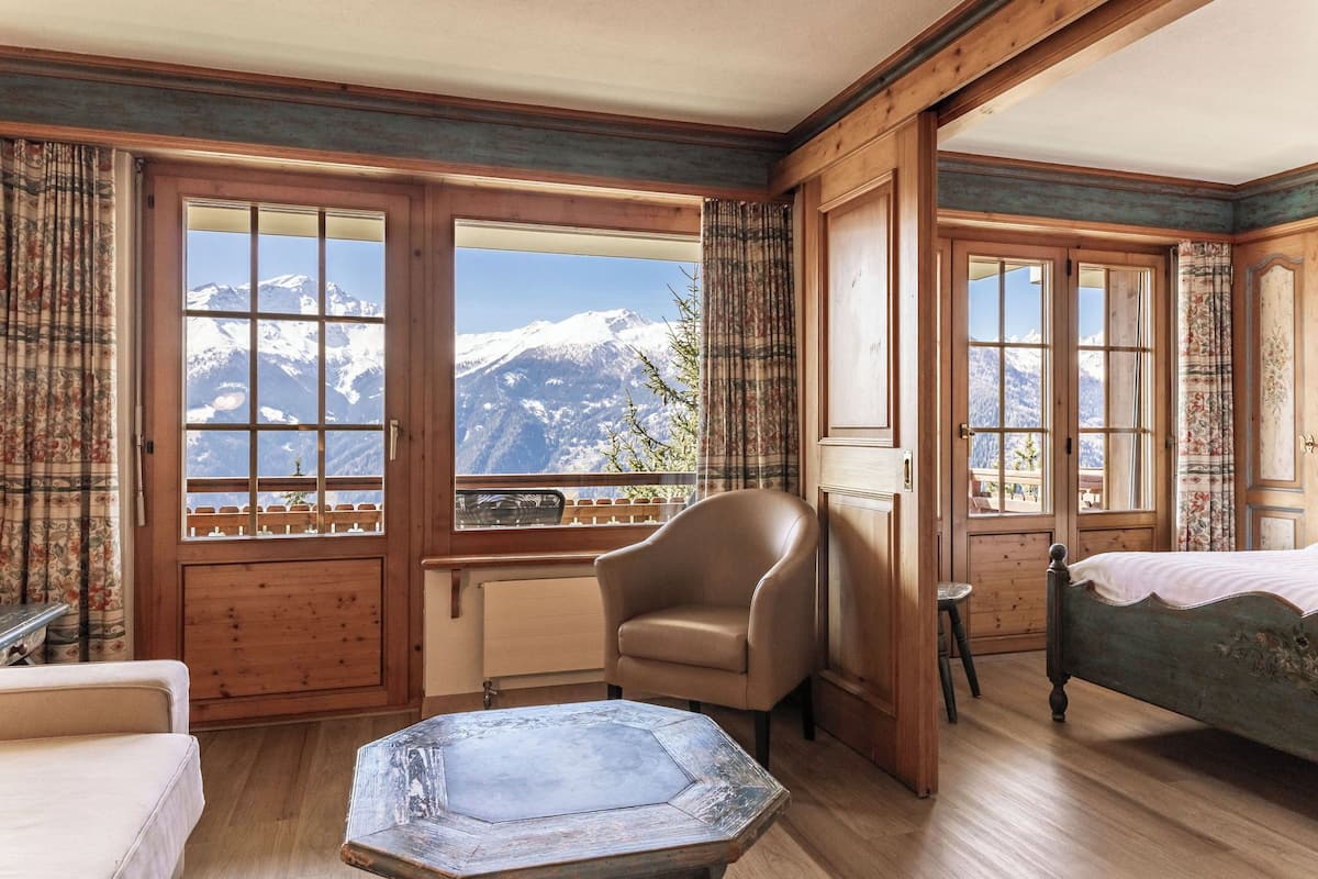 Una habitación con paredes de madera, un ventanal con vistas a la montaña, una cama, una silla y una mesa.