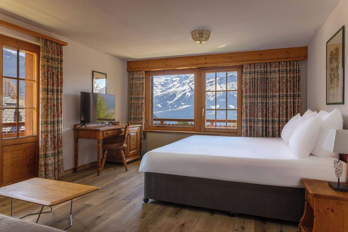 Habitación de hotel con una cama grande, un escritorio de madera, una silla y un televisor.