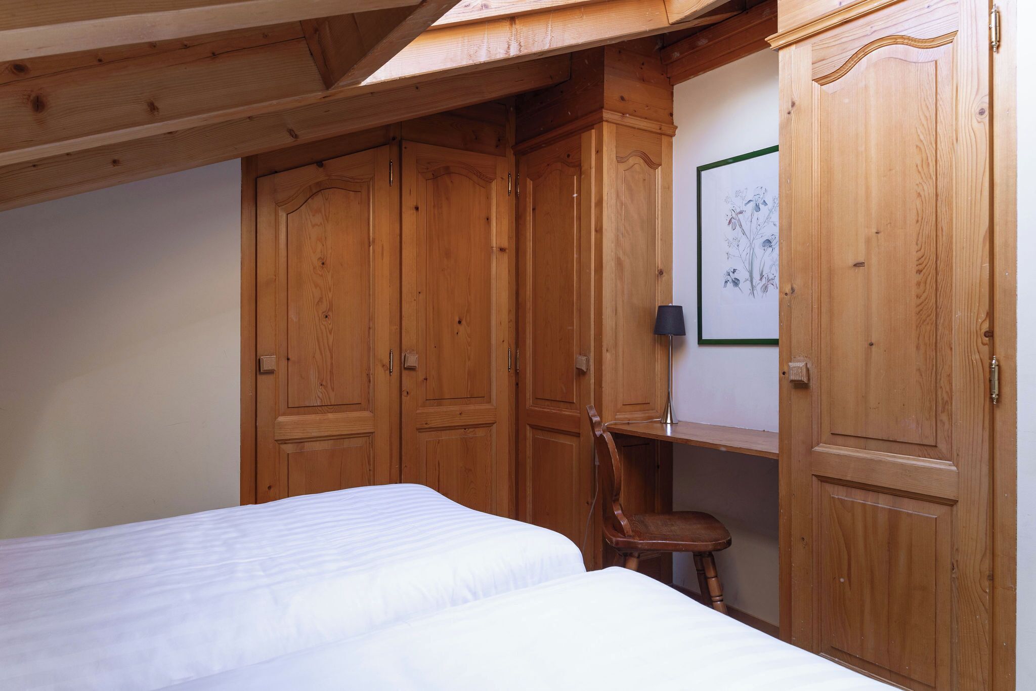 A bedroom with wooden wardrobes, a bed, a desk, and a chair.