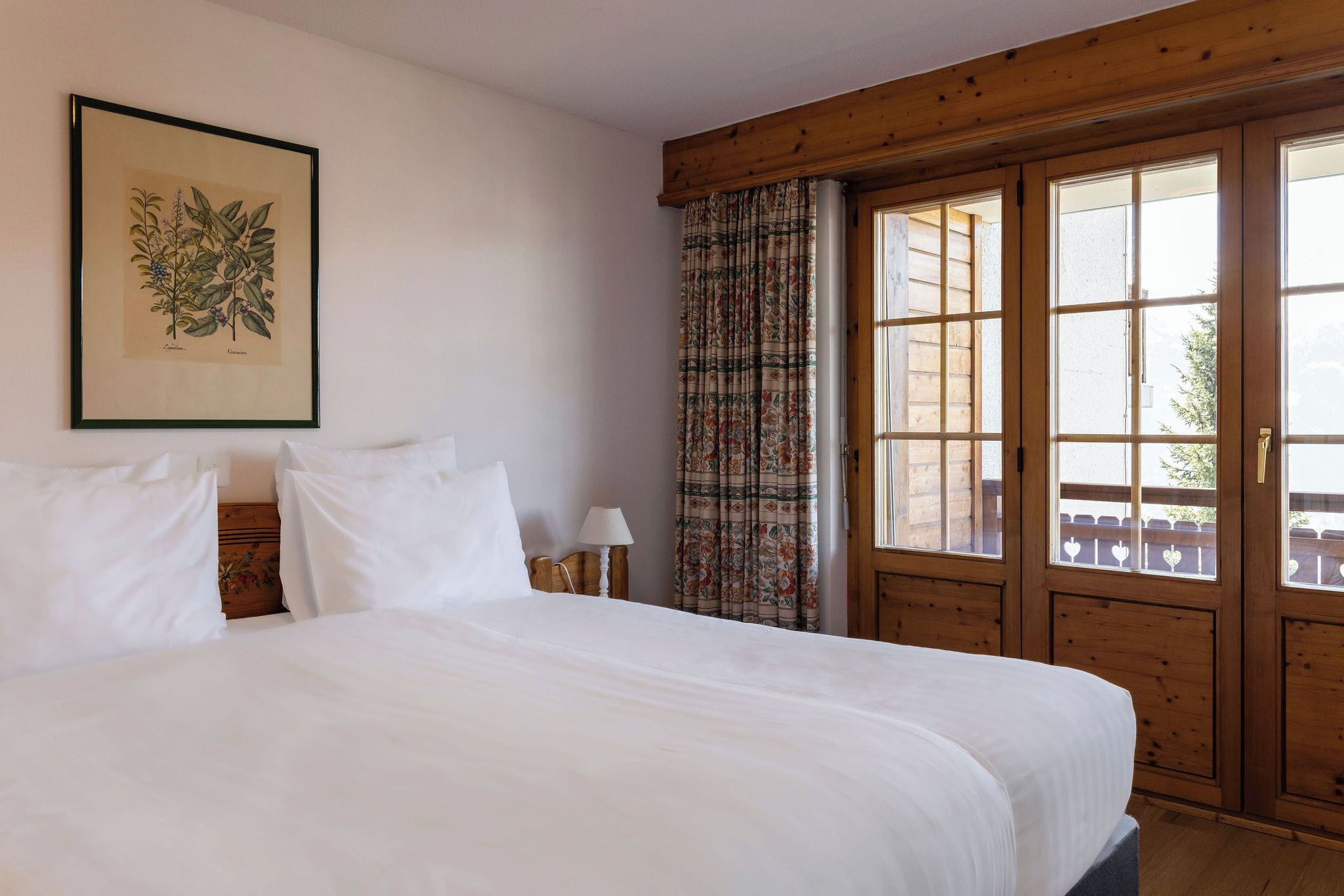 A large bed with white linens, a wooden headboard, a nightstand with a lamp, and a window with curtains.