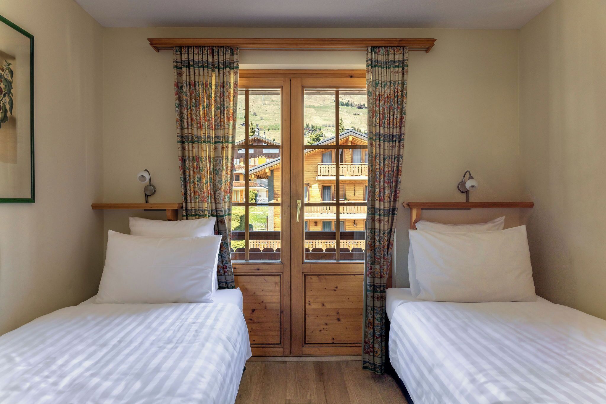 Une chambre avec deux lits, des portes en bois et une vue sur un immeuble doté de balcons.