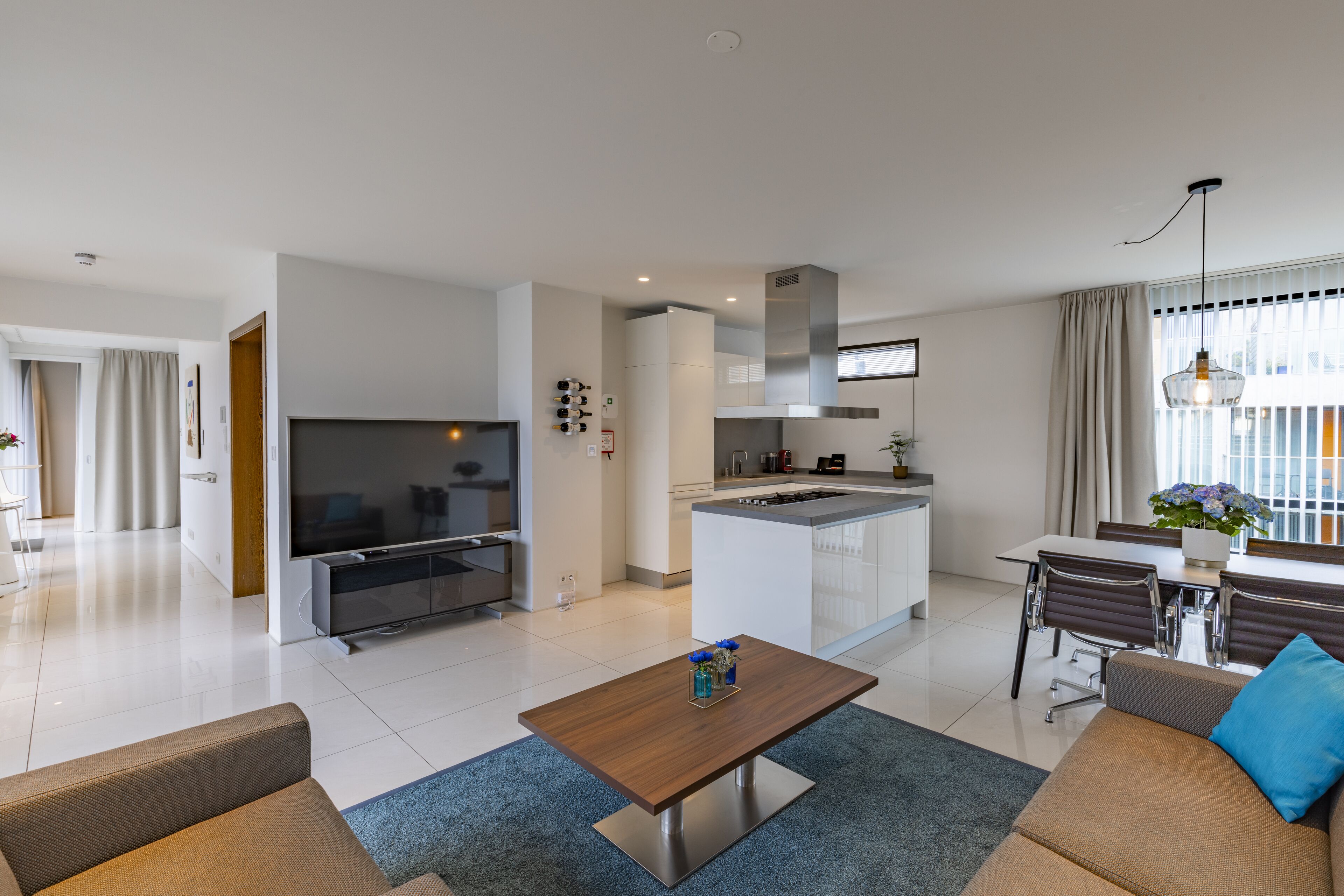 A modern living room with a TV, sofa, coffee table, and dining area with chairs.