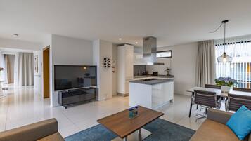 A modern living room with a TV, sofa, coffee table, and dining area with chairs.