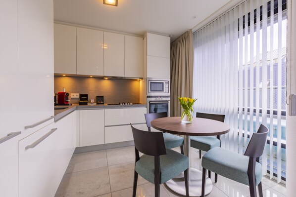 A modern kitchen with white cabinets, a microwave, and a stove. There is a dining area with a round table and chairs.
