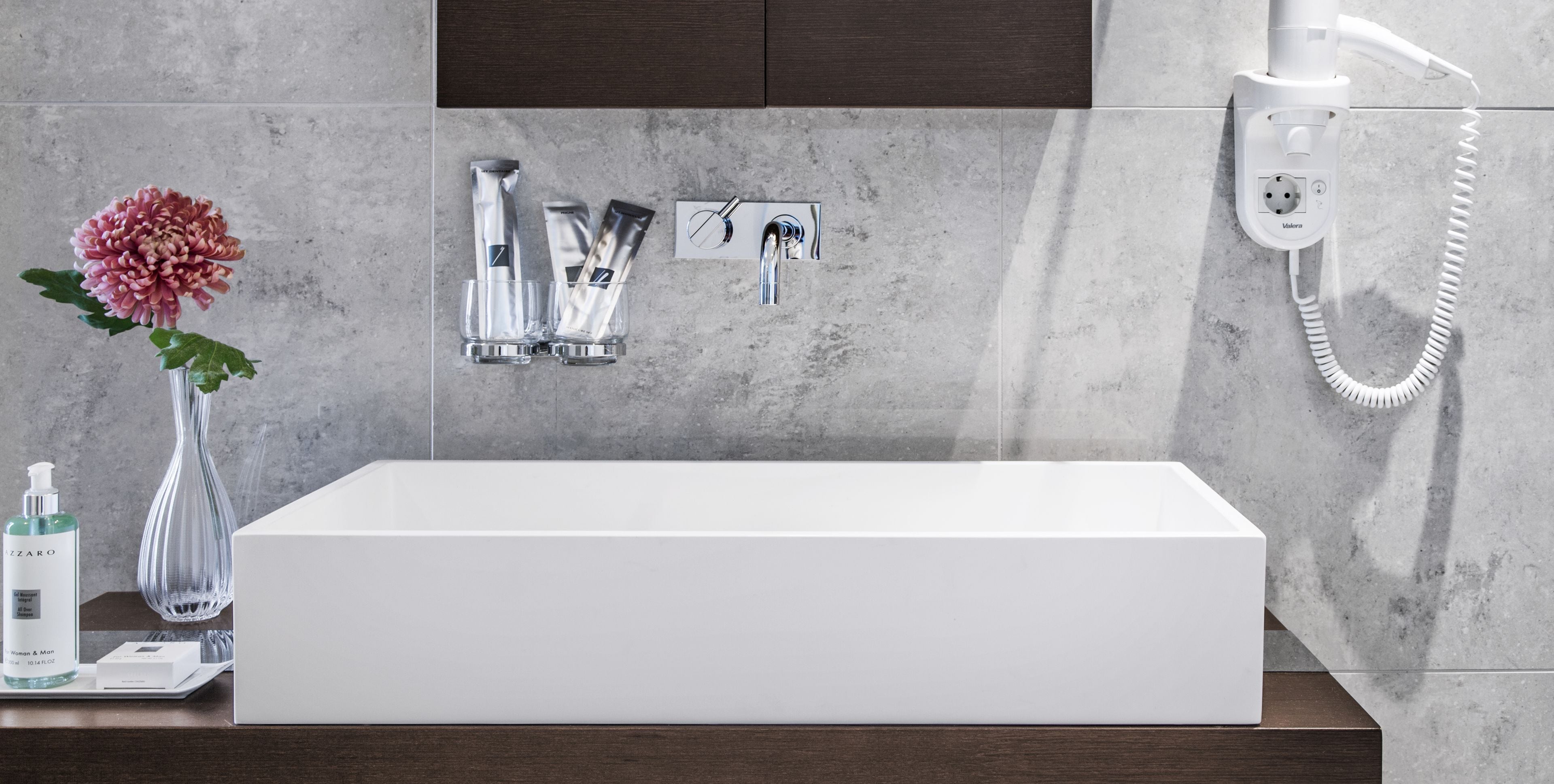 A modern bathroom with a white bathtub, a handheld showerhead, and a hairdryer on a wall-mounted charging station.