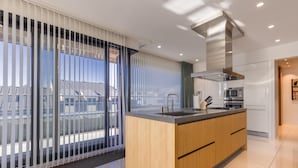 Une cuisine moderne dotée d’un îlot central, d’appareils électroménagers en acier inoxydable et de grandes fenêtres équipées de stores.
