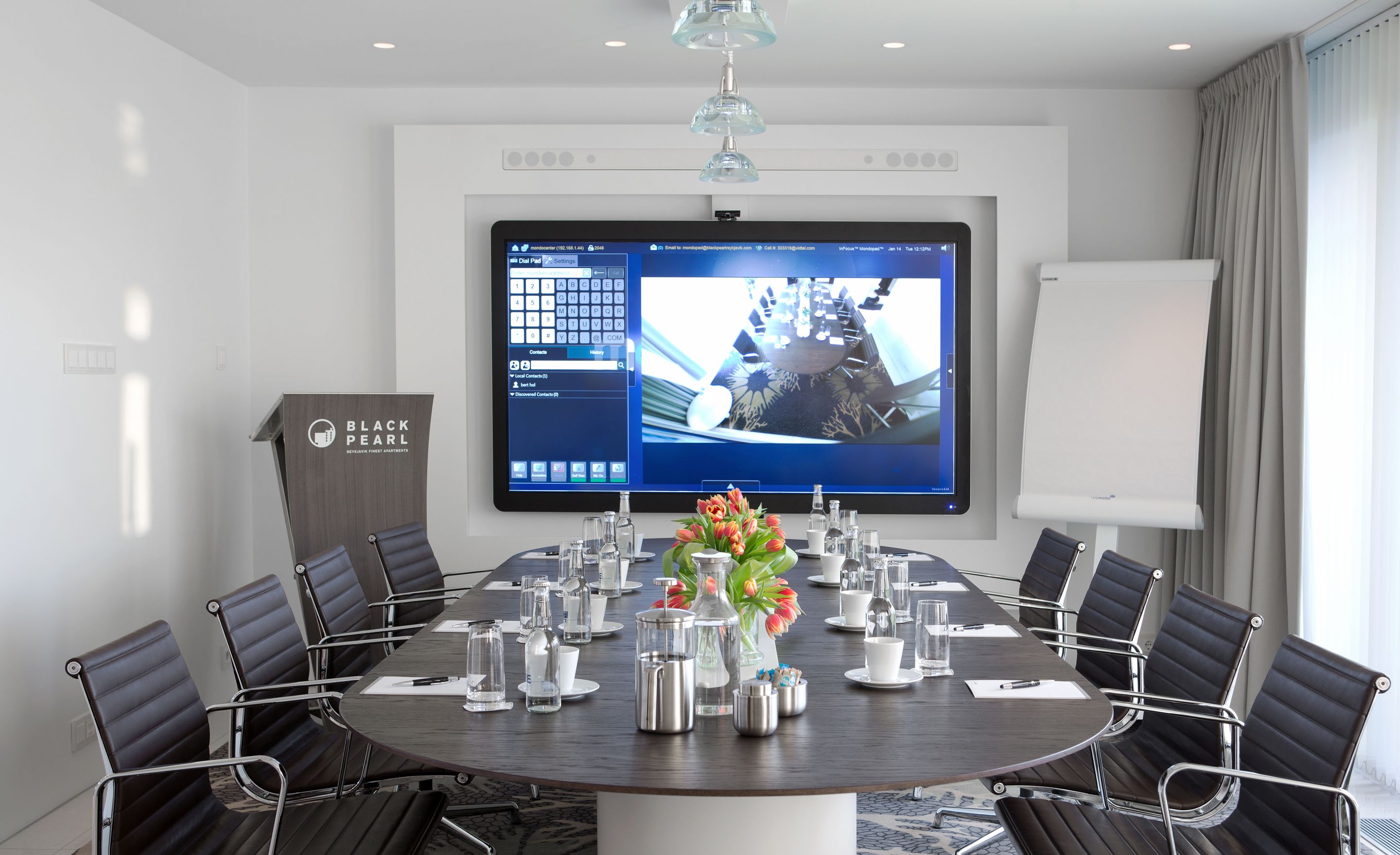 A conference room with a large screen, a whiteboard, and a table set for meetings.