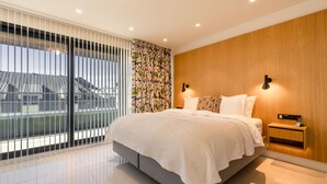 Une chambre à coucher moderne avec un grand lit, un mur d’accent en bois, une table de chevet avec une lampe et une vue dégagée grâce à de grandes fenêtres du sol au plafond.