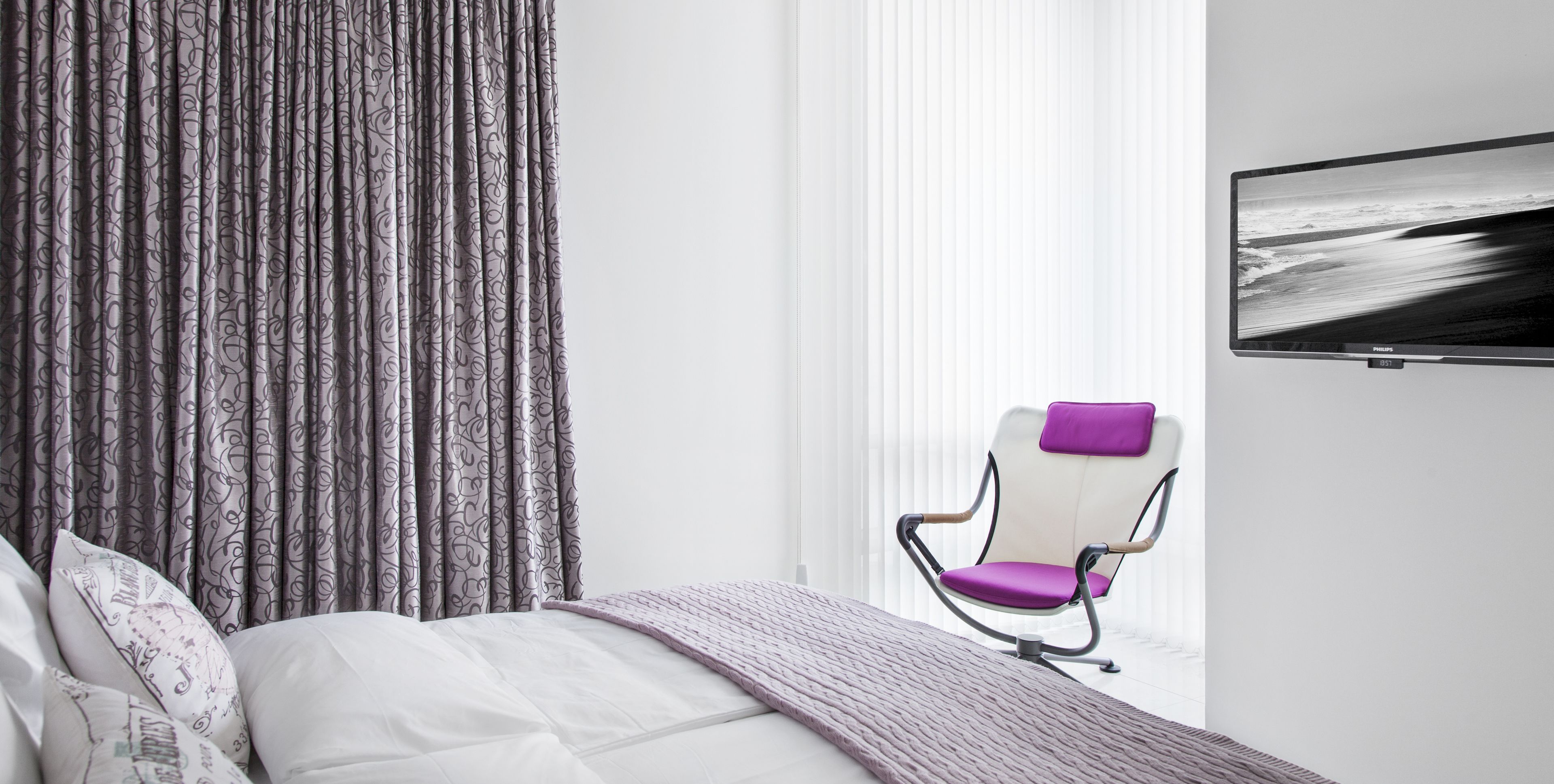 A modern bedroom with a bed, a chair, a TV, and curtains.