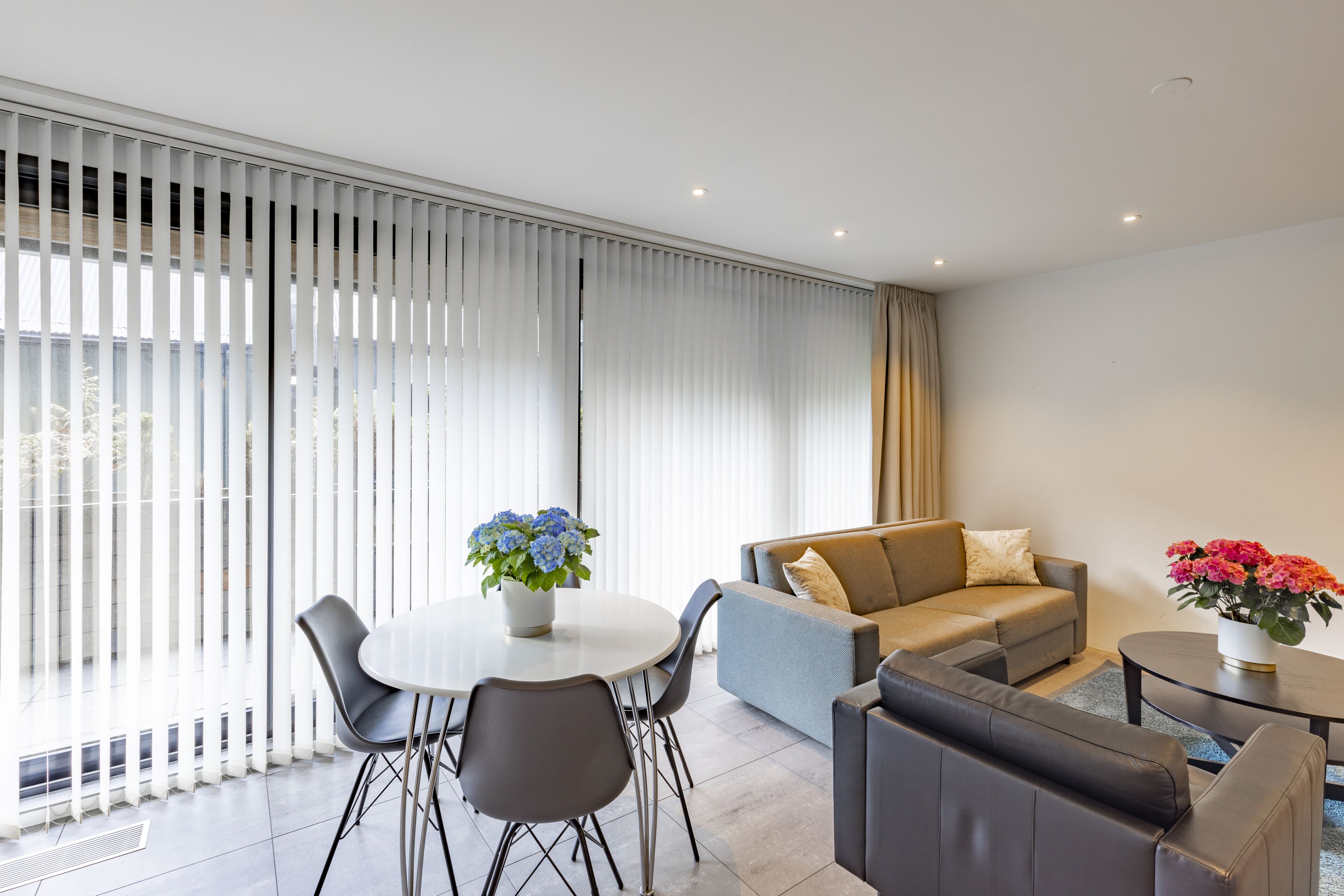 Una sala de estar moderna con una mesa de comedor, un sofá y un ventanal con persianas.