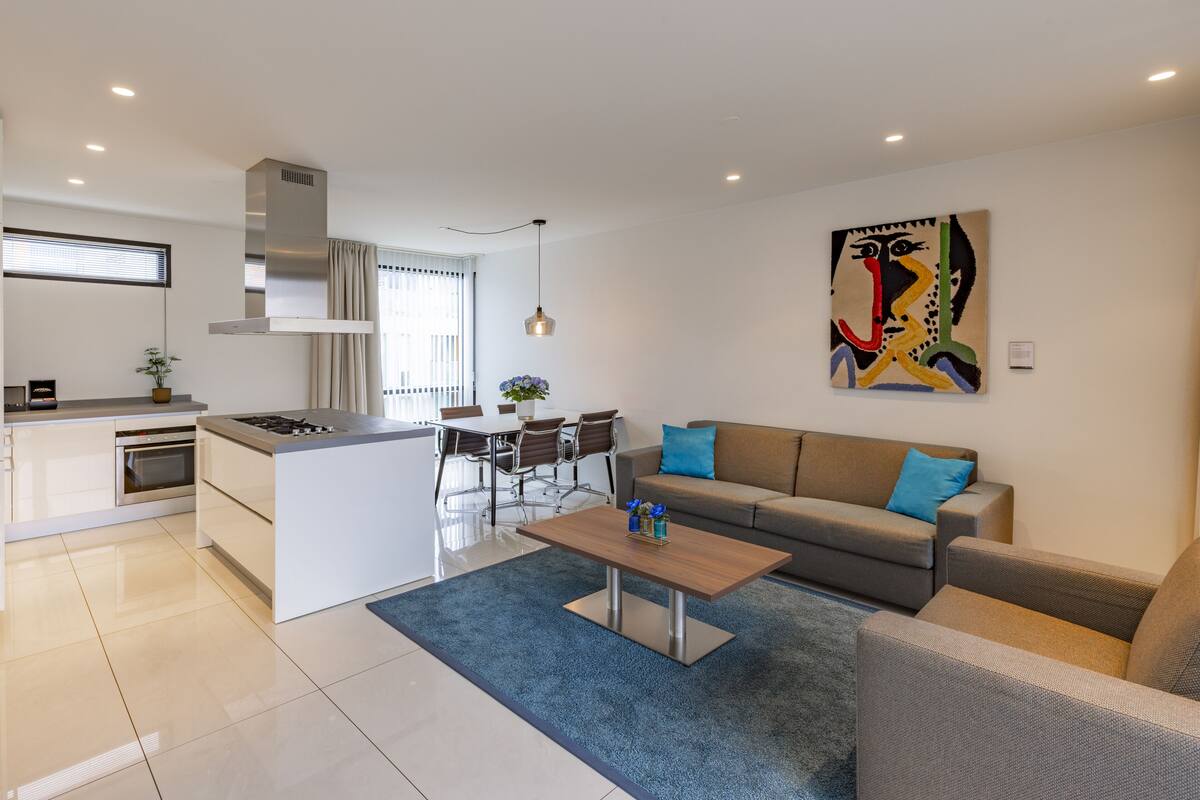 Un apartamento moderno con cocina, comedor y sala de estar. Cuenta con una isla central, un sofá y una mesa de centro.