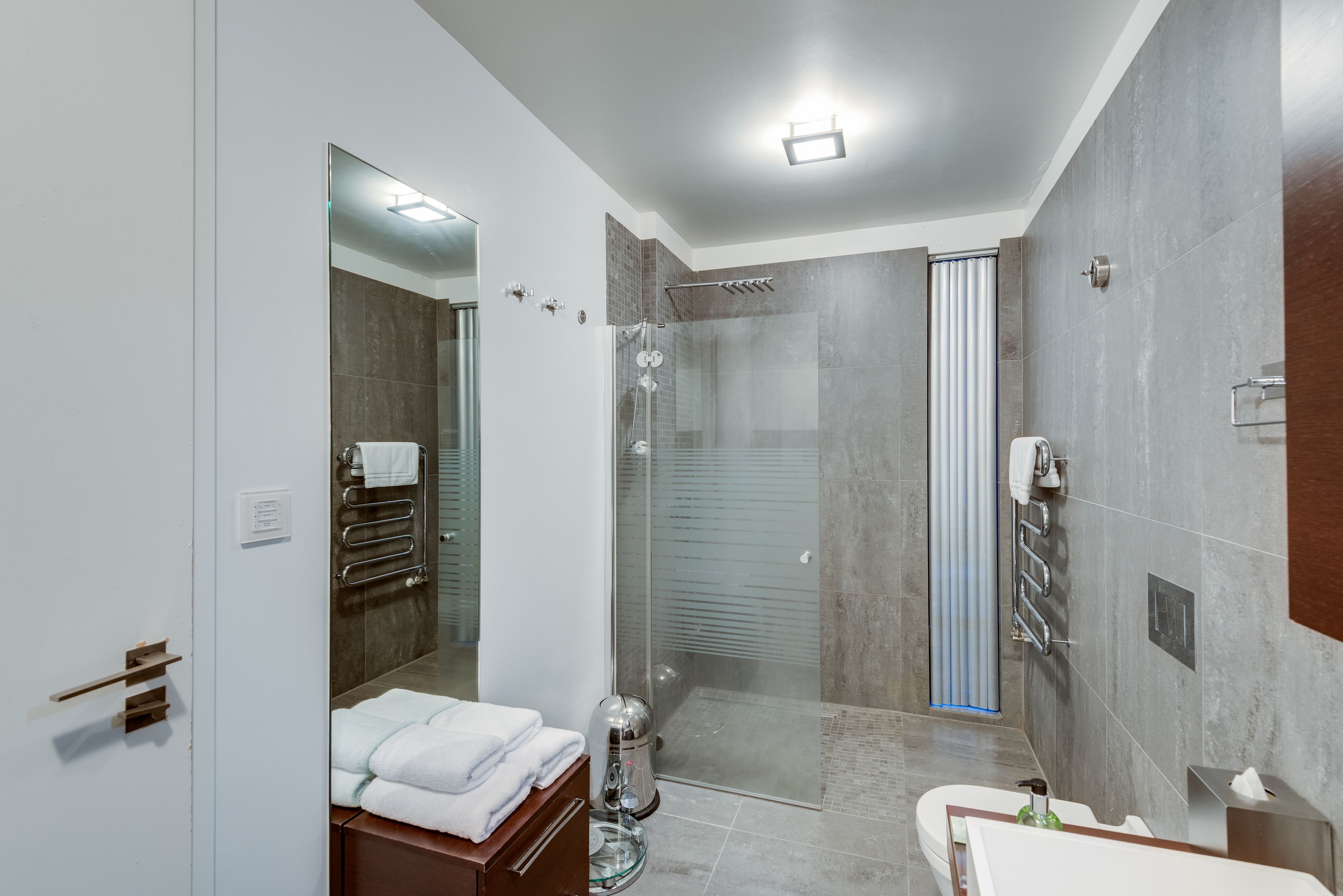 Un bagno moderno con doccia vetrata, uno specchio grande e un mobile lavabo con lavandino e porta asciugamani.