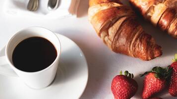 A white cup of coffee on a saucer, two croissants, and strawberries on a white surface.