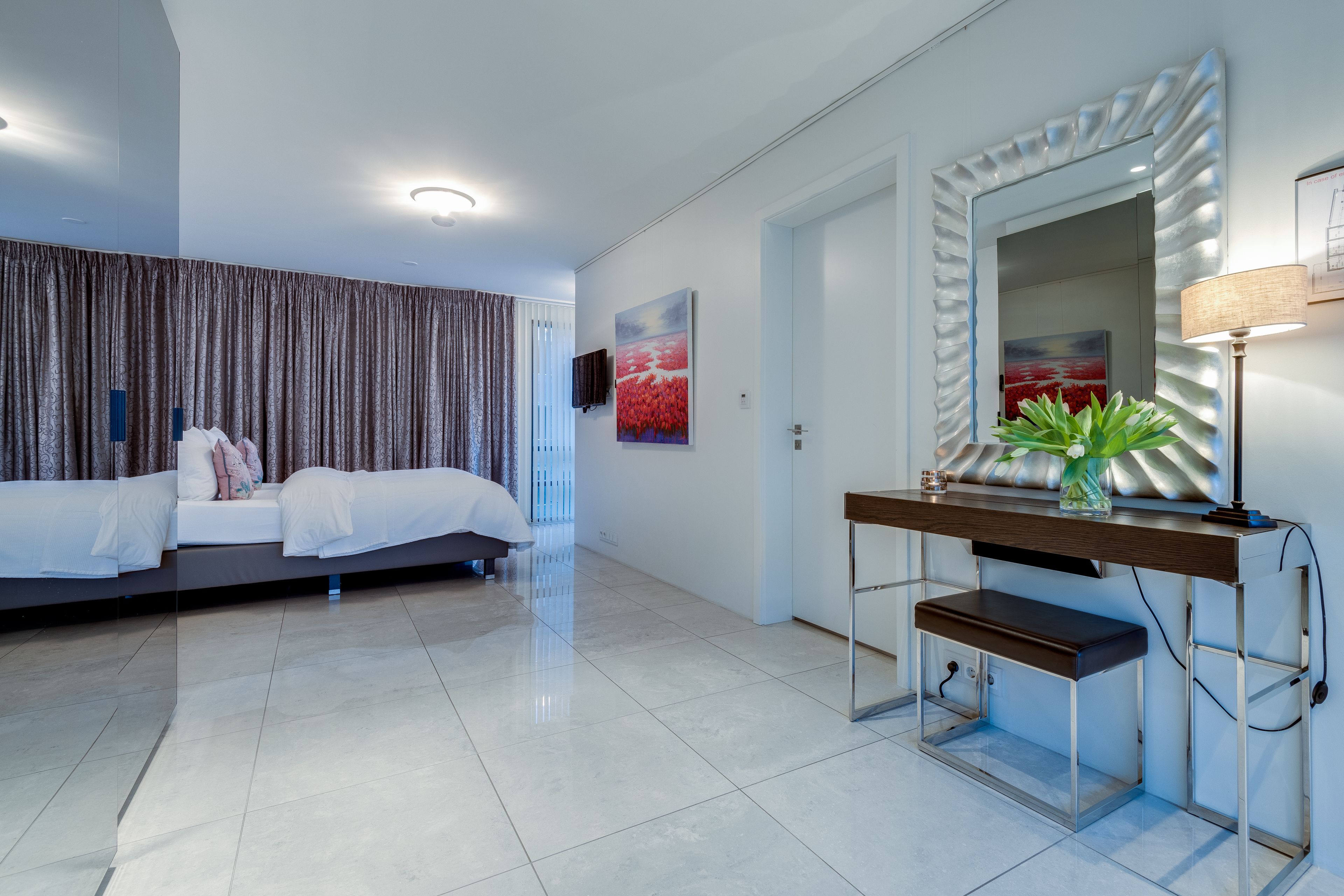Une chambre d’hôtel moderne équipée d’un lit, d’une table de chevet, d’un miroir et d’un téléviseur.